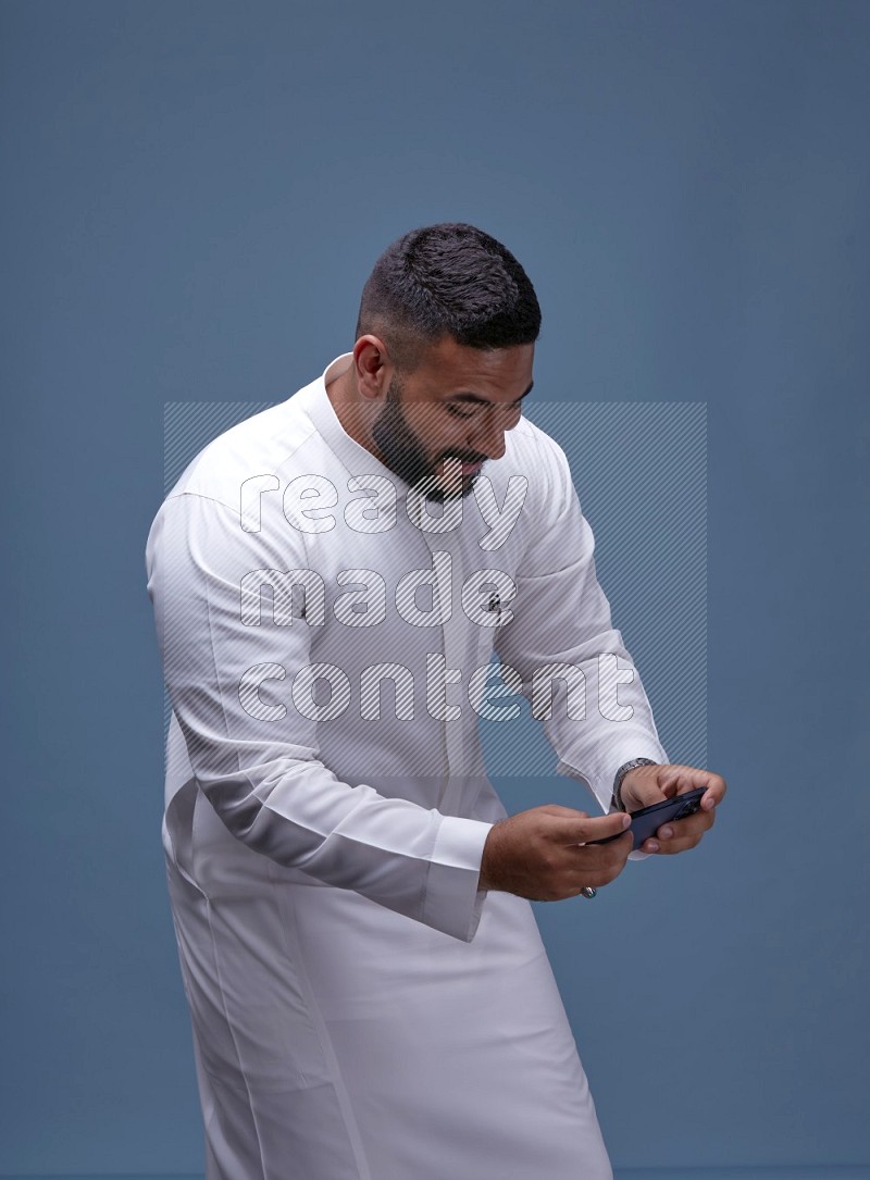 رجل سعودي يرتدي ثوب ابيض ويلعب في جواله
