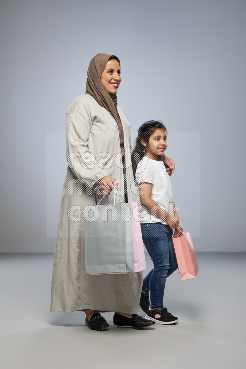 Mom and daughter holding shopping bags on gray background