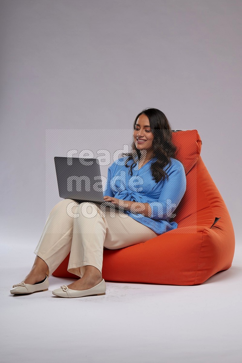 A woman sitting on an orange beanbag and working on laptop
