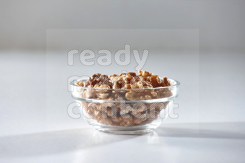 A glass bowl full of peeled walnuts on a white background in different angles
