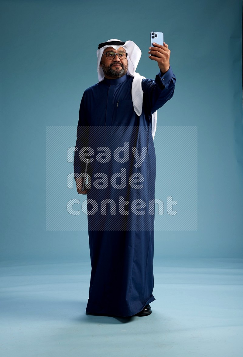 Saudi Man with shimag Standing taking selfie on blue background