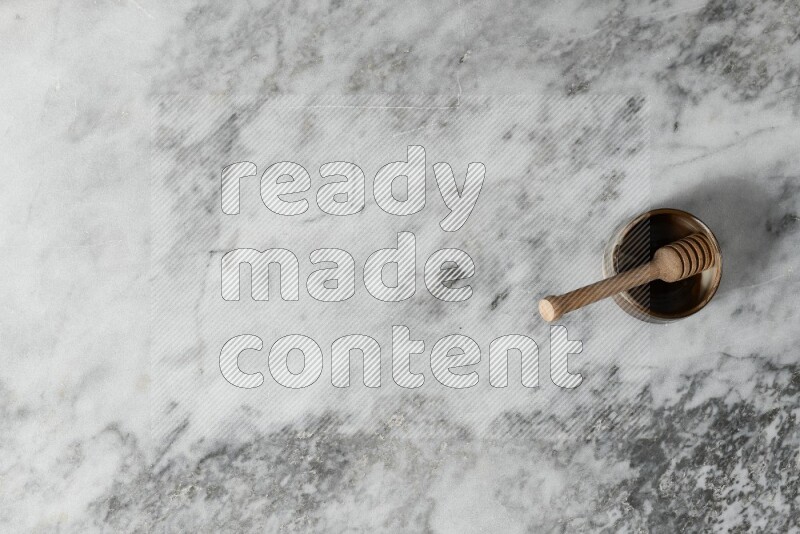 Brown pottery bowl with wooden honey dipper in it on grey marble background