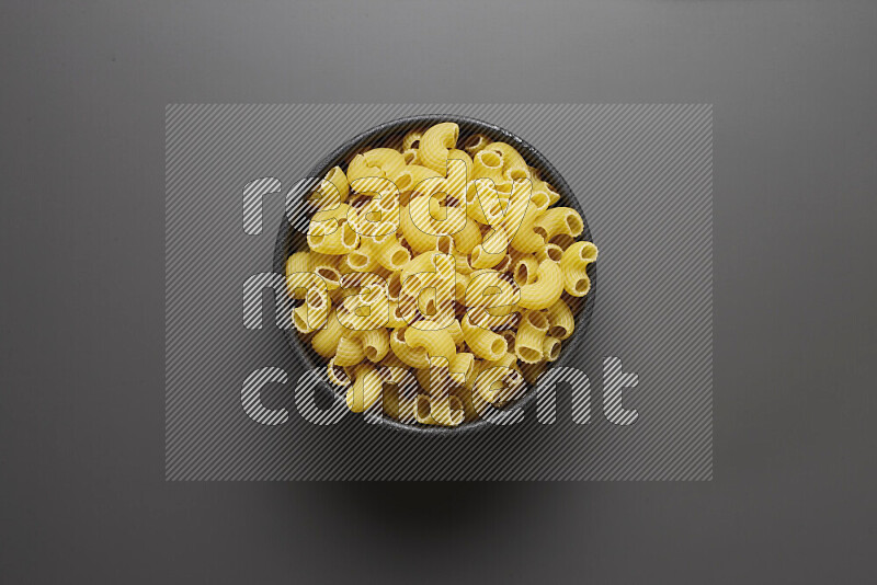 Elbow pasta in a pottery bowl on grey background