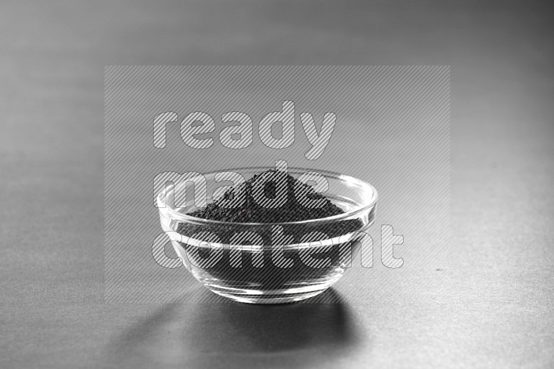 A glass bowl full of black seeds on black flooring