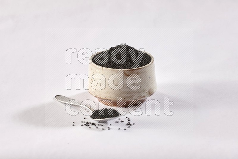 A beige pottery bowl and a metal spoon full of black seeds and more seeds spread on a white flooring in different angles