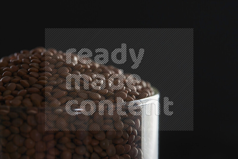 Brown lentils in a glass jar on black background