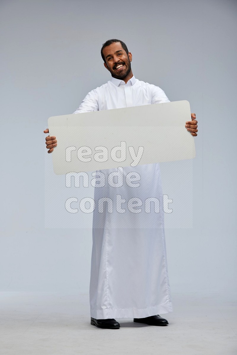 Saudi man wearing Thob standing holding board on Gray background