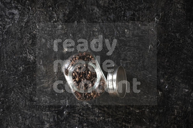 A glass spice jar full of cloves on textured black flooring