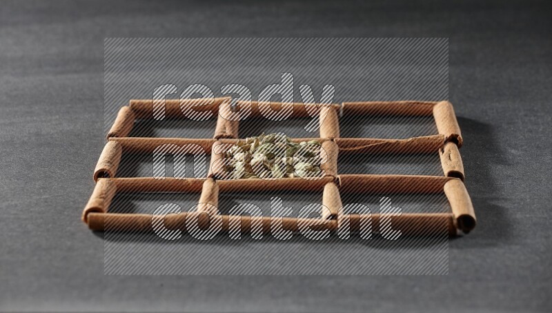 9 مربعات من أعواد القرفة ممتلئة بالهيل في المنتصف محاطة بجوزة الطيب والقرفة وأوراق الغار والقرنفل والكمون والزنجبيل المجفف والريحان المجفف واليانسون على أرضية سوداء