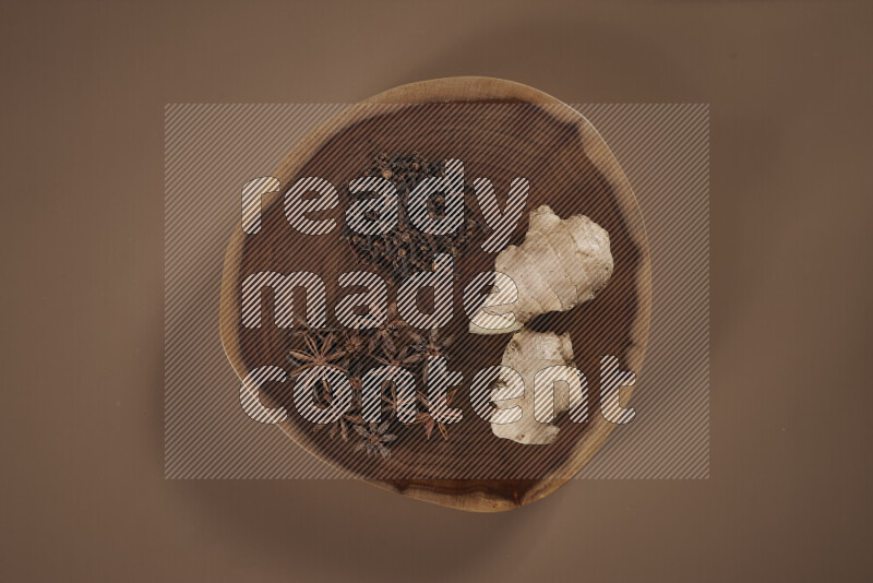 An assorted whole spices on a flat wooden tray including fresh and dried ginger, cinnamon sticks, cardamom, turmeric fingers, cloves, star anise on beige background