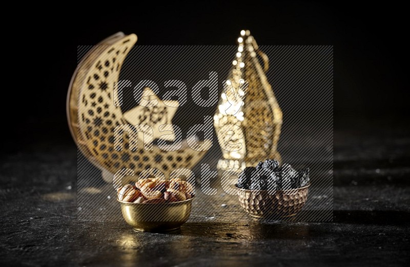 Nuts in a metal bowl with dried plums beside golden lanterns in a dark setup