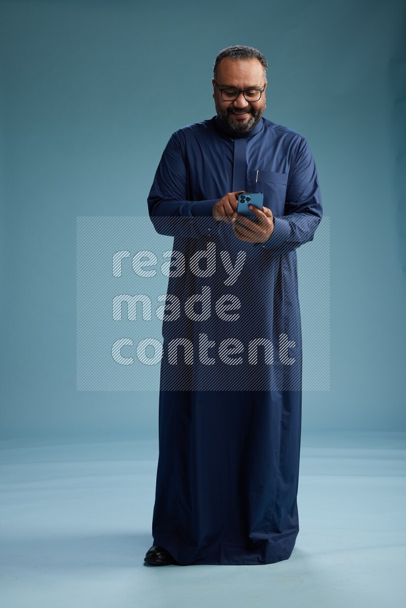 Saudi Man without shimag Standing texting on phone on blue background