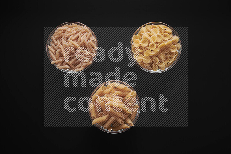 Different pasta types in glass bowls on black background