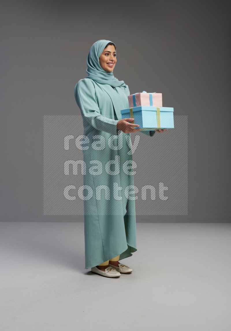 Saudi Woman wearing Abaya standing holding gift box on Gray background