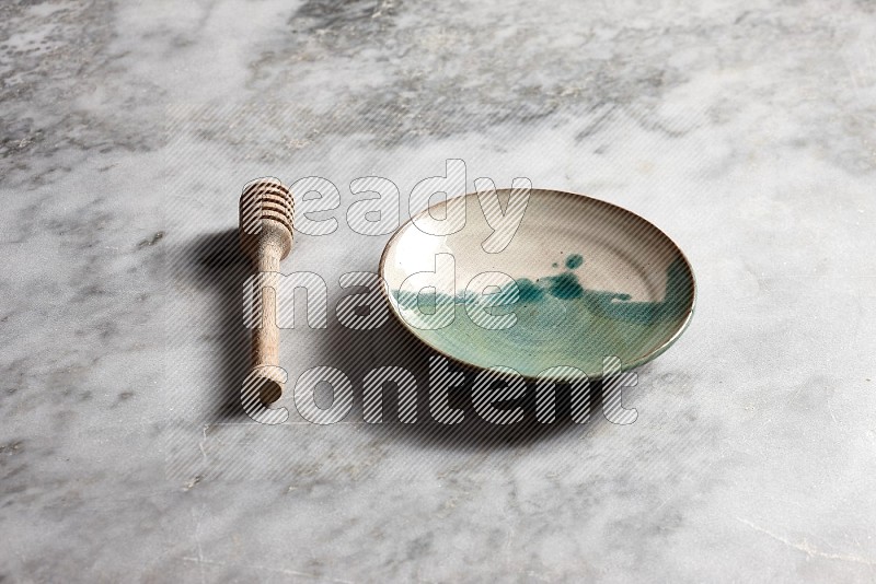 Multicolored Pottery Plate with wooden honey handle on the side with grey marble flooring, 45 degree angle