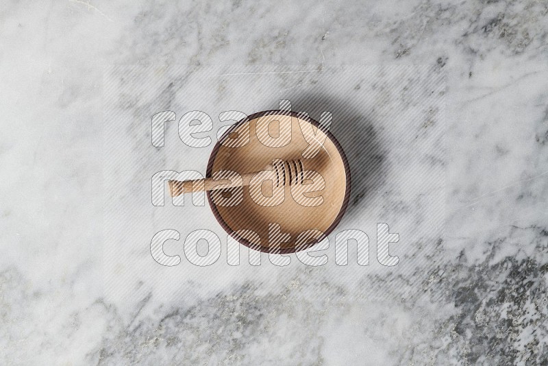 Beige Pottery Oven Plate with wooden honey handle in it, on grey marble flooring, Top View