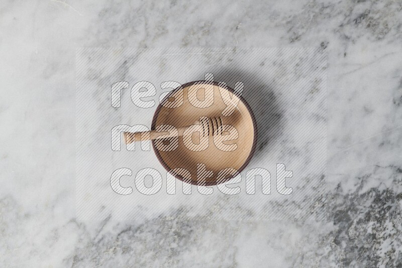 Beige pottery oven plate with wooden honey dipper in it on grey marble background