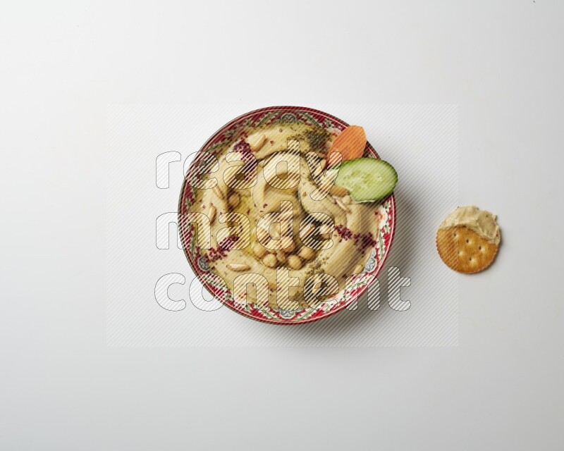 Hummus in a red plate with patterns garnished with zaatar & sumak on a white background