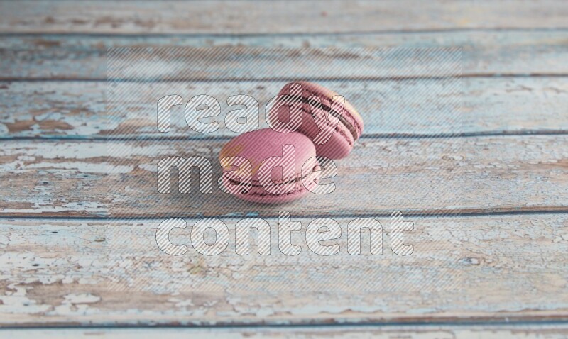 45º Shot of two Purple Strawberry macarons on light blue wooden background