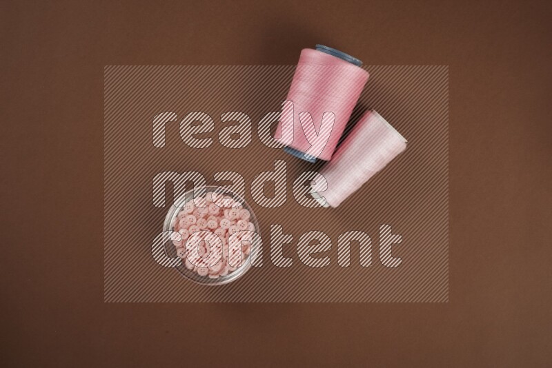 مجموعة من أدوات الخياطة والتفصيل زهرية اللون على خلفية بنية