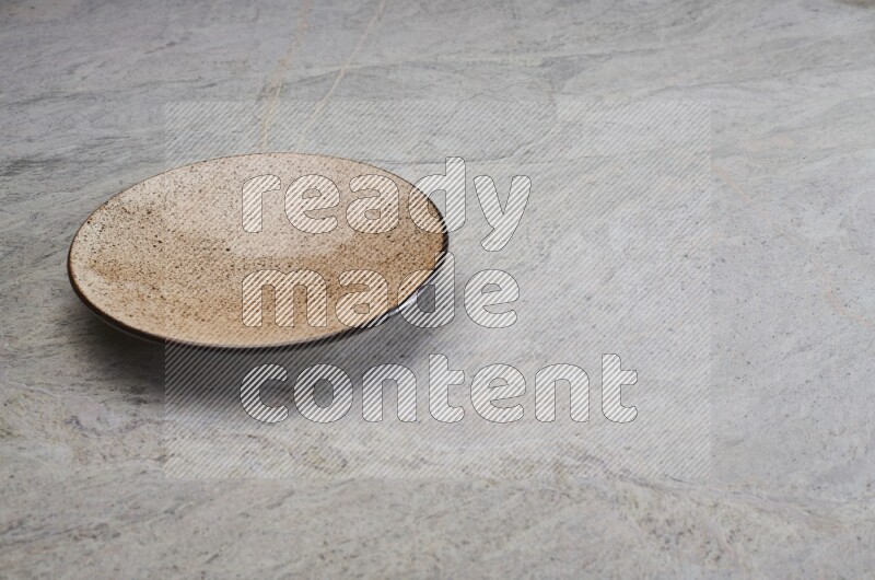 A beige pottery plate on grey marble background