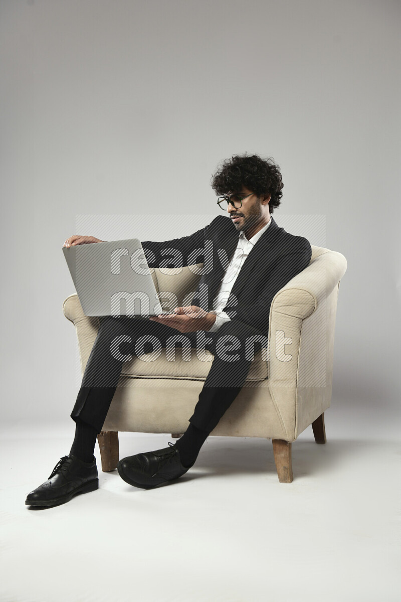 A man wearing formal sitting on a chair working on a laptop on white background