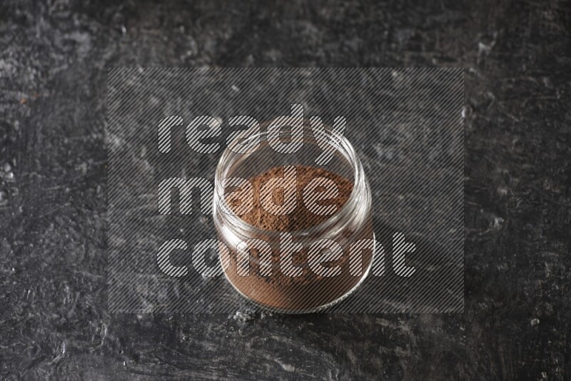 A glass jar full of cloves powder on a textured black flooring
