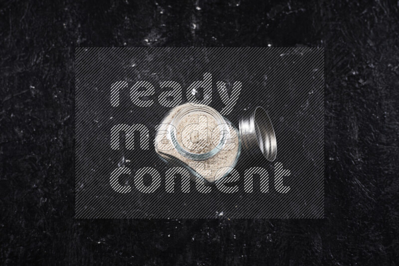 A glass jar full of onion powder on black background