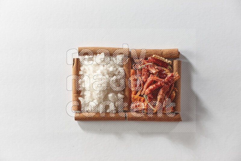 مربعان من أعواد القرفة ممتلئان بالفلفل الحار المجفف والملح الأبيض علي خلفية بيضاء