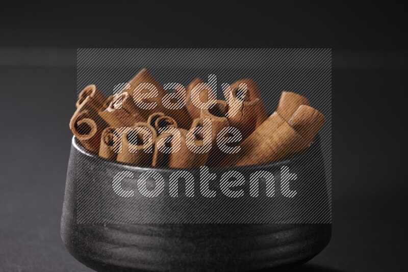 Cinnamon sticks in a black bowl on a black background in different angles