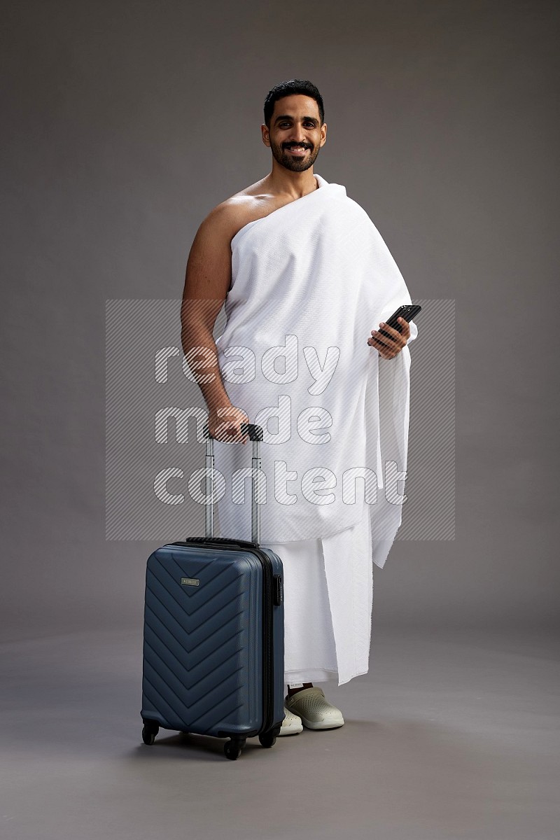 A man wearing Ehram Standing holding traveling bag on gray background