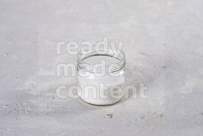 A glass jar full of fine table salt on white background