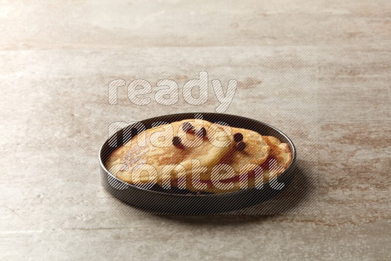 Three stacked chocolate chips pancakes in a black plate on beige background