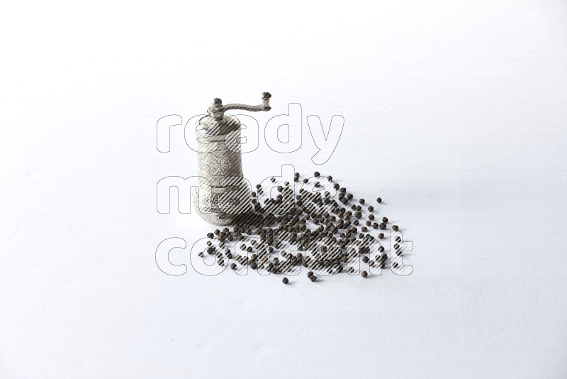 A turkish metal pepper grinder and spreaded black pepper beads on a white flooring
