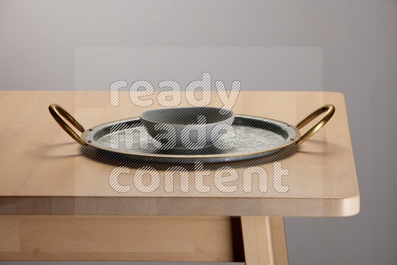 grey bowl placed on a rounded stainless steel tray with golden handels on the edge of wooden table