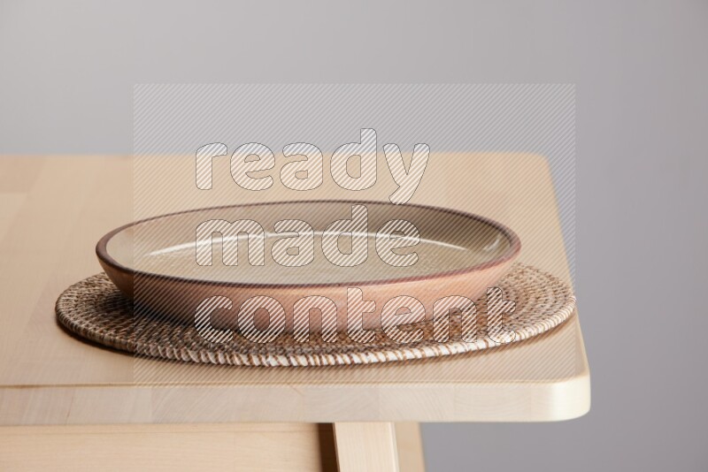 multi-colored pottery Plate placed on a big light colored straw placemat on the edge of wooden table