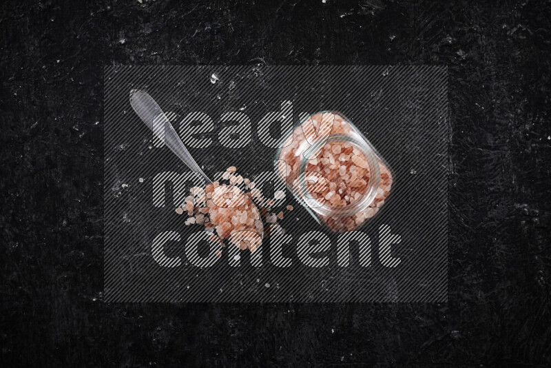 A glass jar full of coarse himalayan salt crystals on black background