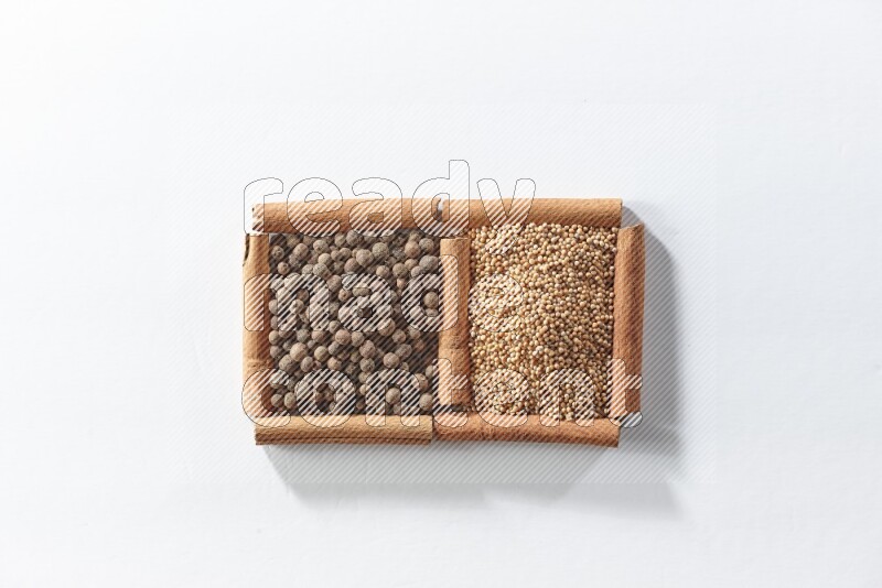 مربعان من أعواد القرفة ممتلئان بحبوب الخردل وحبوب بهار الفلفل الحلو علي خلفية بيضاء