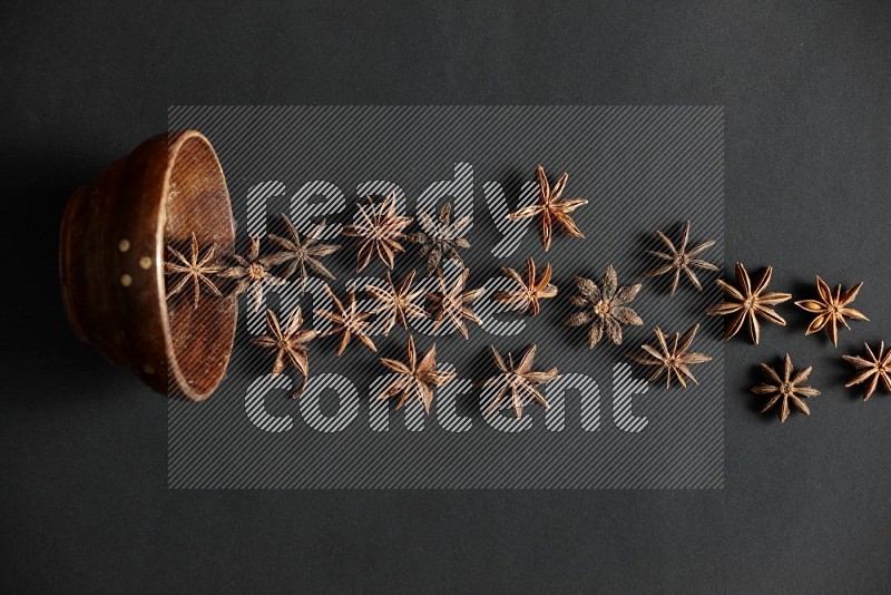 Star anise lined out of wooden bowl across the frame on black background