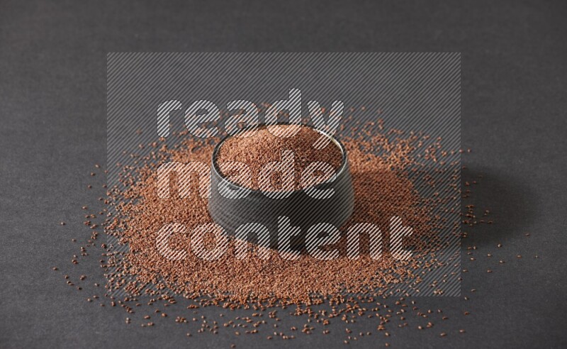 وعاء فخاري أسود ممتلئ ببذور حب الرشاد محاط بالبذور على أرضية سوداء