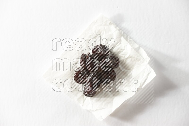 Dried plums on a crumpled piece of paper on a white background in different angles