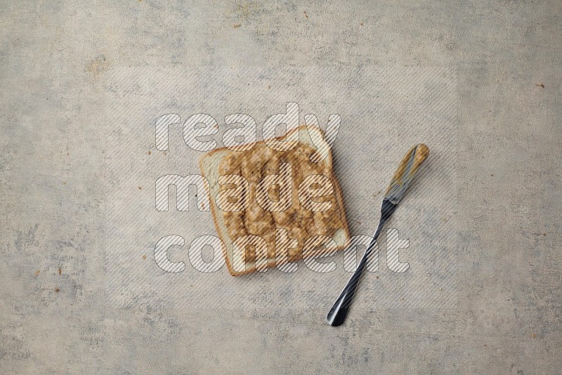 crunchy peanut butter on a white toast with a spreading knife on a light blue textured background