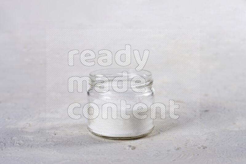 A glass jar full of fine table salt on white background