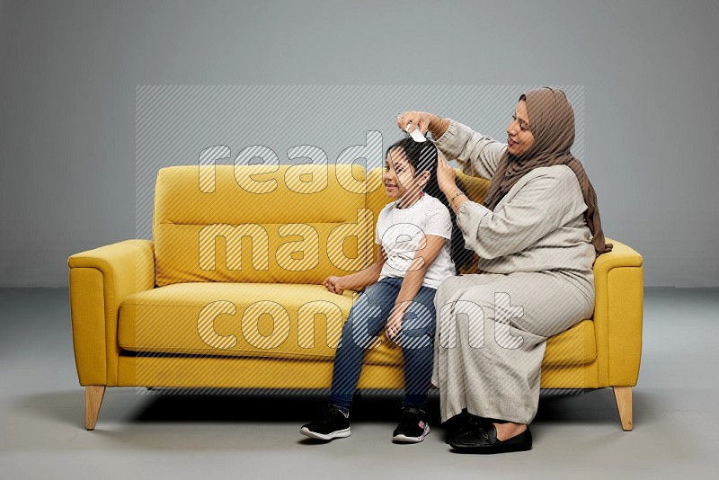 A mother sitting styling hair for her daughter on gray background