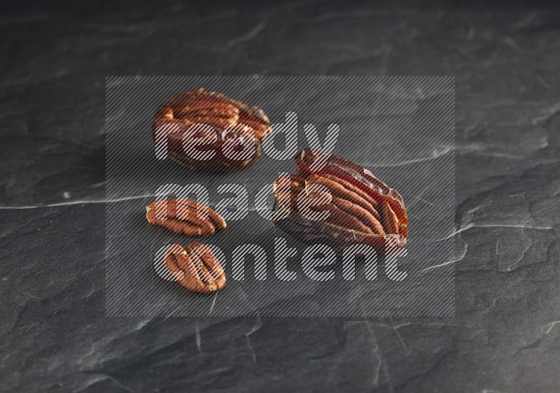 two pecan stuffed madjoul dates on a black textured background