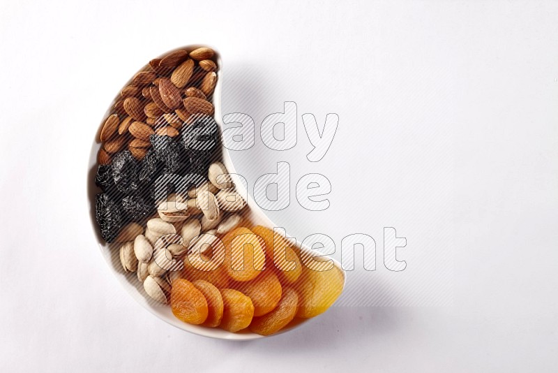 Mixed nuts and dried fruits in a crescent pottery plate on white background