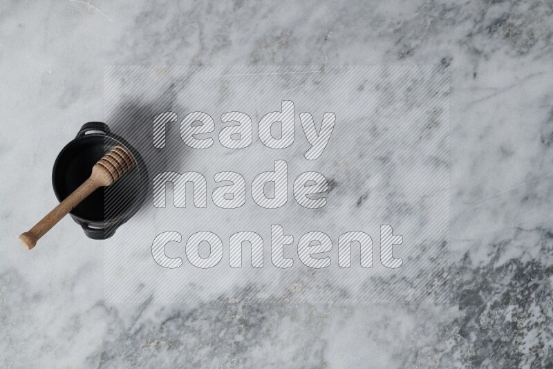 Black pottery bowl with wooden honey dipper in it on grey marble background