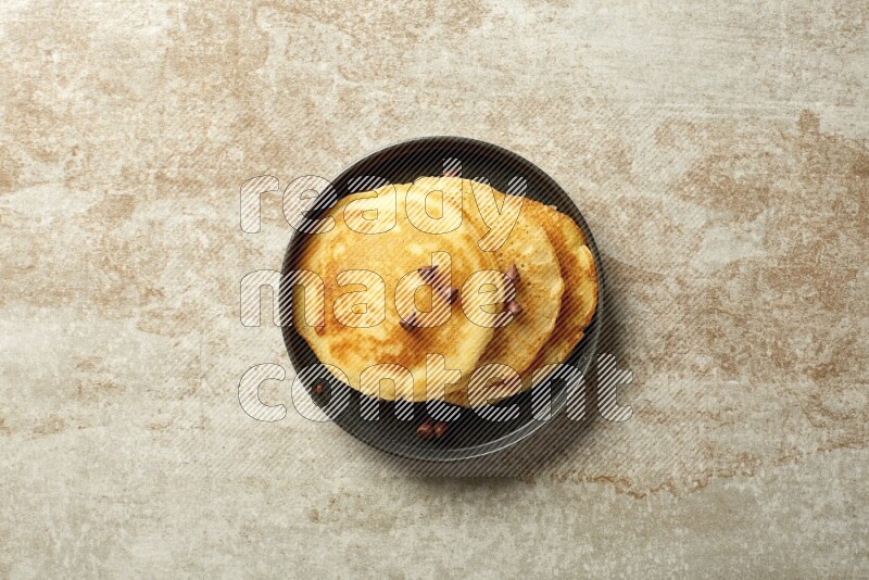 Three stacked chocolate chips pancakes in a black plate on beige background