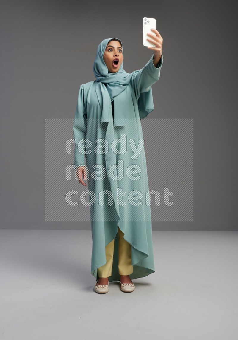 Saudi Woman wearing Abaya standing taking selfie on Gray background