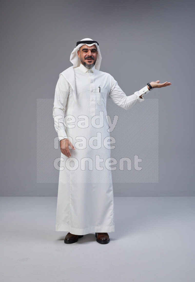 Saudi man Wearing Thob and white Shomag standing interacting with the camera on Gray background